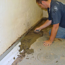 A contractor in West Islip installing a perimeter drain tile system during a sump pump installation.